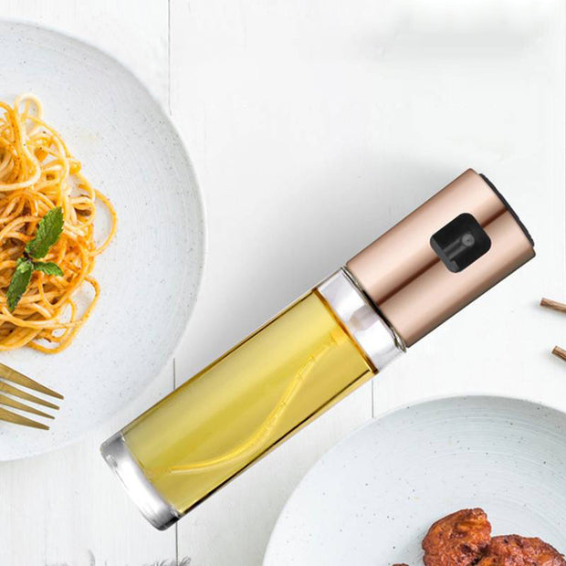 Oil vinegar spray bottle with golden liquid next to pasta and chicken on a white plate.