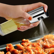 Oil vinegar spray bottle in hand spraying oil over grilled chicken on a barbecue.