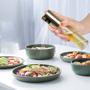 Oil vinegar spray bottle dispensing oil over fresh salads and dishes in kitchen settings.