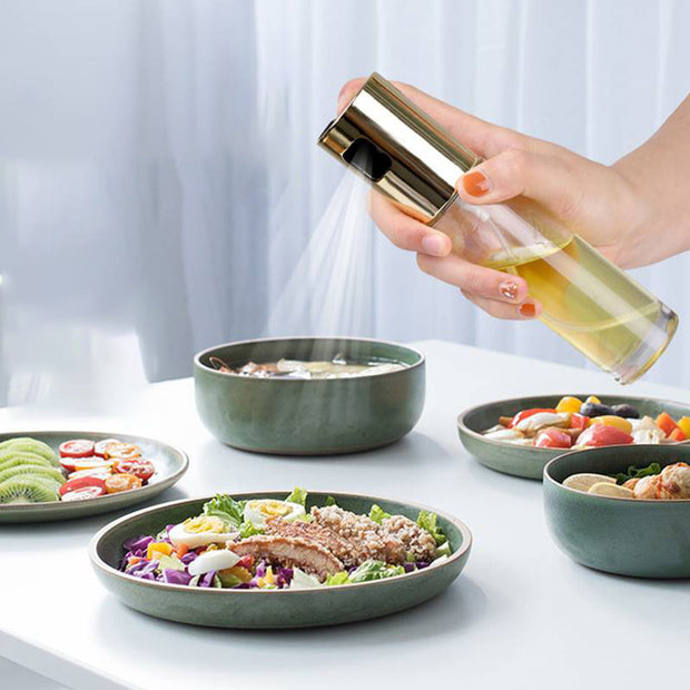 Oil vinegar spray bottle dispensing oil over fresh salads and dishes in kitchen settings.