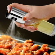 Hand holding an oil vinegar spray bottle, spraying oil onto grilled chicken on a barbecue.