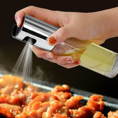 Hand holding an oil vinegar spray bottle, spraying oil onto grilled chicken on a barbecue.