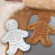 Image of skull shape biscuit mold with skeleton cookies on a baking surface, perfect for Halloween treats.