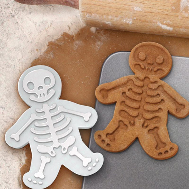 Image of skull shape biscuit mold with skeleton cookies on a baking surface, perfect for Halloween treats.